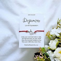 a red string bracelet with a silver heart charm on it and flowers in the background