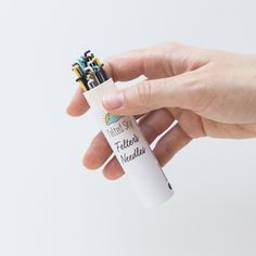 a hand holding a small white tube with writing on it and several pencils sticking out of it