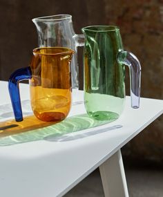 three different colored glass vases sitting on a white table with shadows coming from them