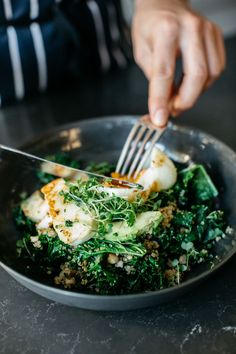 a person holding a fork in a bowl filled with greens and eggs on top of a table