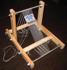 a wooden weaving machine on a table with wires attached to the loom and thread