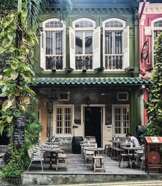 the outside of a restaurant with tables and chairs in front of it, surrounded by greenery