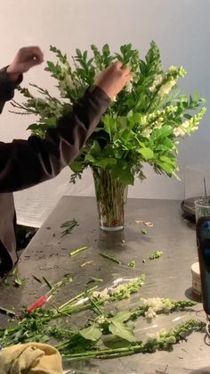 a man is arranging flowers in a vase on a table with other things around him