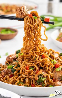 noodles with meat and vegetables being lifted by chopsticks from a white bowl on a table