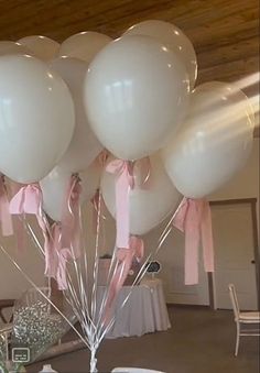 a bunch of white balloons with pink ribbon tied to them in a room filled with tables and chairs