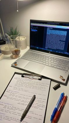 an open laptop computer sitting on top of a desk next to a pen and paper