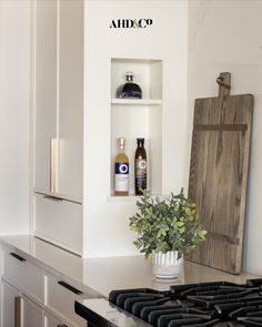 a kitchen with white cabinets and an open shelf above the stove top, filled with bottles