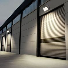 an industrial building with shuttered doors and lights on the side of it at night