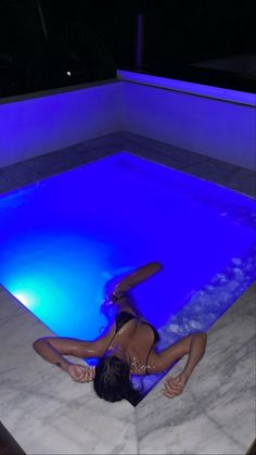 a woman in a bathing suit is floating in an indoor swimming pool with blue lights