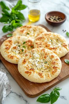 four flat breads on a cutting board with basil leaves and olive oil in the background