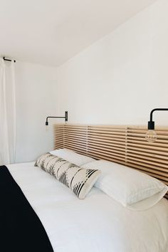 a bed with white sheets and pillows in a bedroom next to a wall mounted light