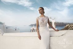 a woman in a white wedding dress standing on a ledge next to the ocean and looking off into the distance