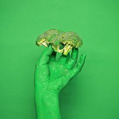 a person's hand holding up a piece of broccoli with green paint on it