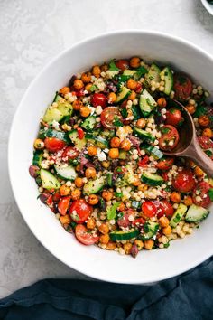 a white bowl filled with vegetables on top of a blue cloth and a wooden spoon