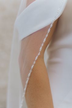 a woman wearing a wedding dress and veil with pearls on the back of her arm