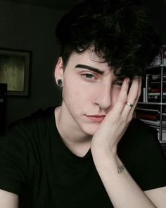 a young man with piercings on his nose sitting in front of a book shelf