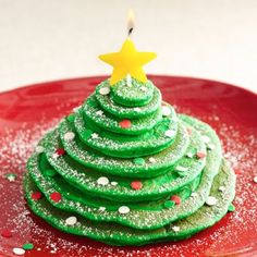 a small green christmas tree on a red plate with sprinkles and a lit candle