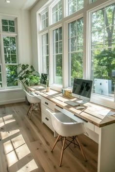 a desk with two computers on it in the middle of a room filled with windows