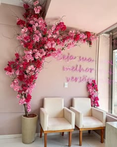 two white chairs sitting next to a pink wall with flowers hanging from it's sides