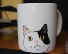 a white coffee mug with a black and white cat face on it's side