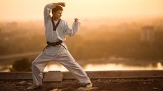 a man doing karate on top of a building with the sun setting in the background