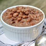 a white bowl filled with beans sitting on top of a blue and white napkin next to a spoon