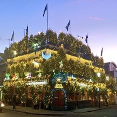 a building covered in christmas lights with flags on the roof and trees all around it