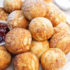 powdered sugar covered pastries on a white plate with dipping sauce in the background