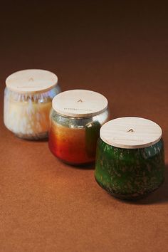 three jars with lids are sitting on a brown surface, one is filled with liquid and the other has something in it