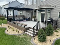 a deck with patio furniture and landscaping in front of a gray house on a cloudy day