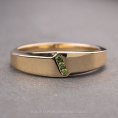 a yellow gold wedding band with two green stones in the center, on a gray surface