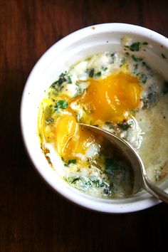 an egg and cheese soup in a white bowl with a spoon on a wooden table