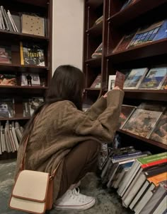 a woman sitting on the floor in front of a bookshelf holding a cell phone