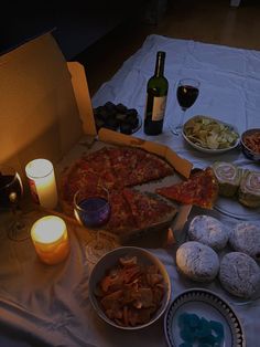 a table topped with pizza and other foods next to wine glasses on top of a white cloth