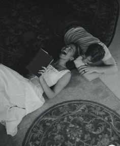 two people laying on the floor next to each other with a book in their hands