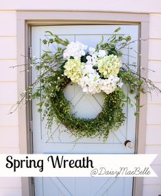 a wreath with white flowers and greenery is hanging on the front door of a house