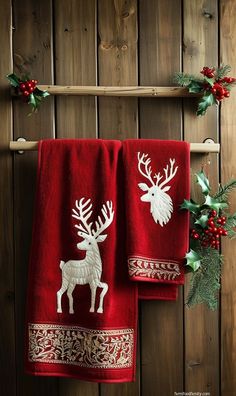 two red towels with white reindeers on them hanging from a wooden wall next to holly wreath