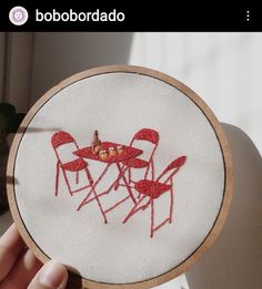 someone is holding up a small embroidery hoop with three chairs and a table on it