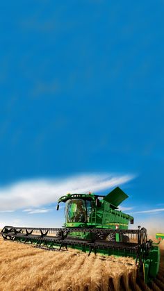 a large green tractor is driving through the wheat field in front of a blue sky