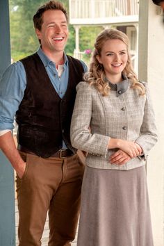 a man and woman standing next to each other on a porch smiling at the camera