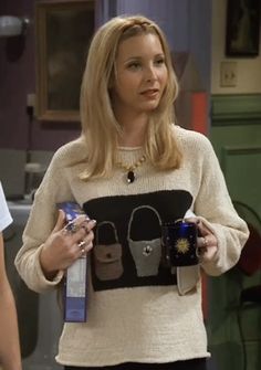 the young woman is holding two cups in her hands and wearing a sweater with purses on it