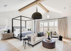 a large bedroom with white walls and wood flooring has a four poster bed in the center