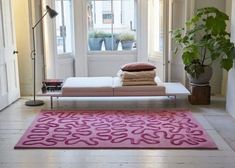 a living room with a pink rug and white couch in the corner next to a potted plant