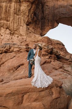 a bride and groom standing in front of a rock formation at the base of a mountain