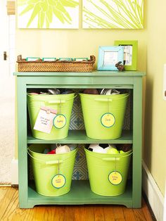 three green buckets sitting on top of a shelf next to a wall with pictures above it