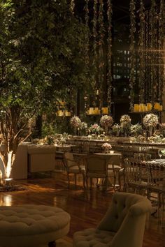 a room with tables, chairs and chandeliers in the middle of it at night