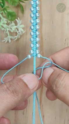 two hands are working on a beaded piece of string that is attached to a wooden table