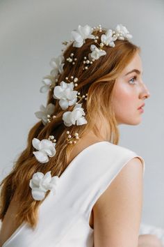 a woman with long hair wearing a white dress and flowers in her hair is looking off to the side