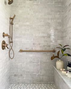 a white tiled bathroom with a shower head and two vases on the shelf next to it