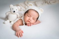 a baby is laying next to a teddy bear on a white blanket with it's eyes closed